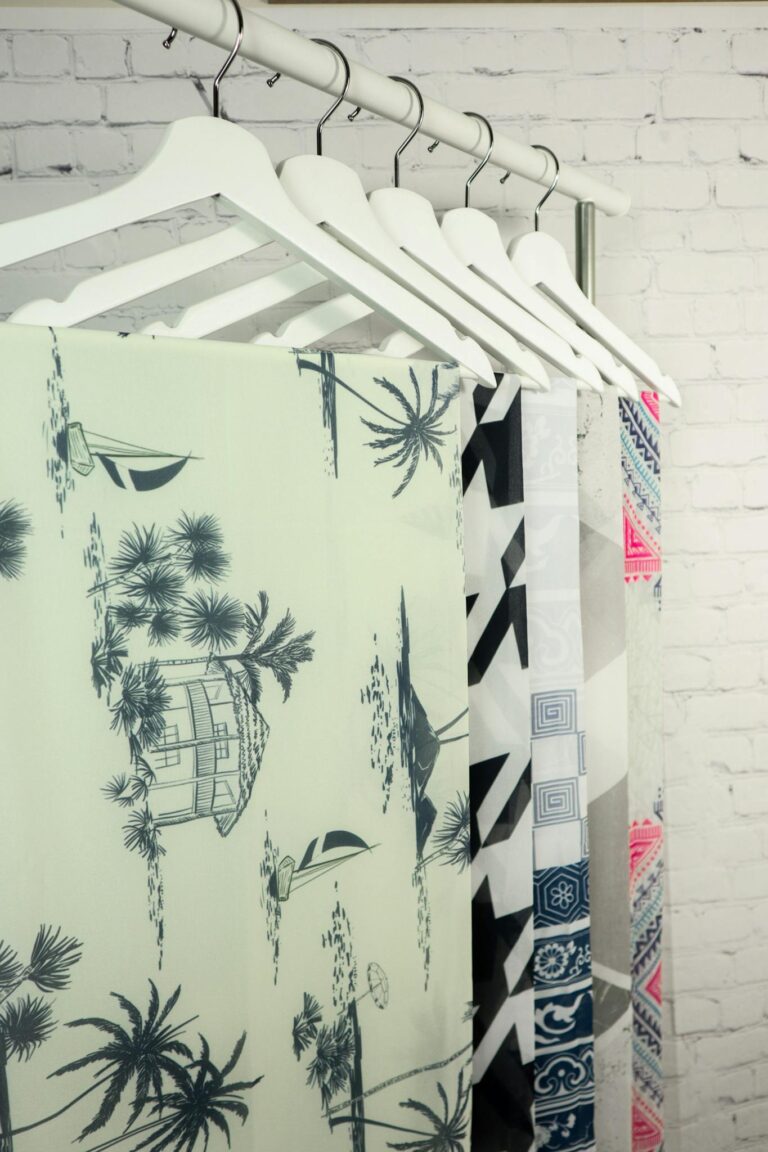 Close-up of various patterned clothes hanging on hangers against a white brick wall.