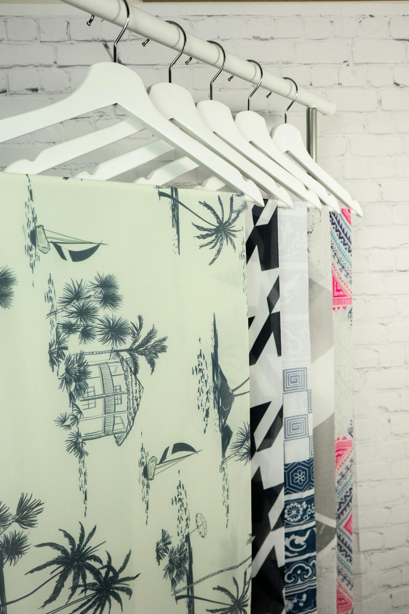Close-up of various patterned clothes hanging on hangers against a white brick wall.