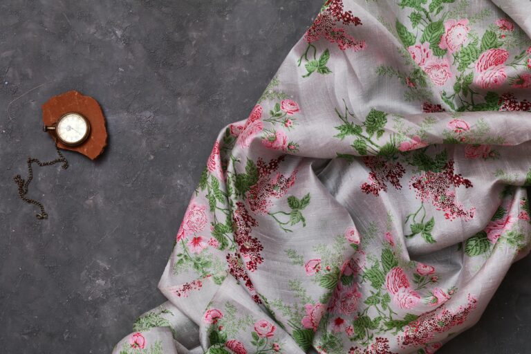 Elegant floral fabric draped beside a vintage pocket watch on a dark surface.